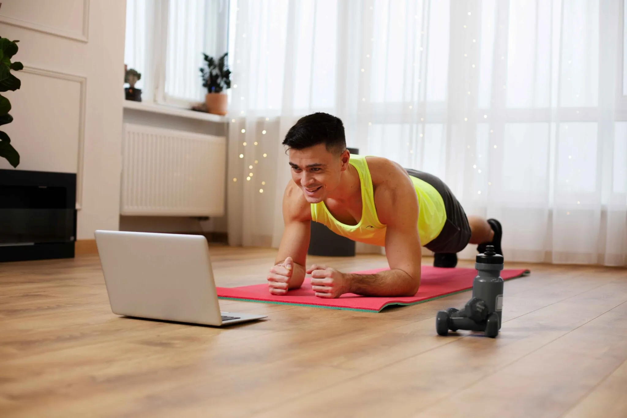 Man doing a plank exercise on a mat at home while following a laptop workout